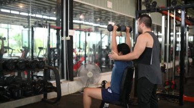 Genç adam spor salonunda antrenörle egzersiz yapıyor.