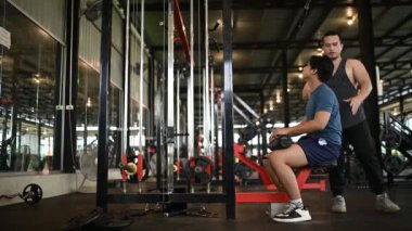 Genç adam spor salonunda antrenörle egzersiz yapıyor.