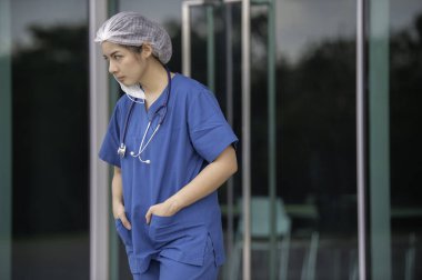 Depresyonda olan Asyalı kadın hemşire yüz maskesi giyiyor mavi üniforma hastane zemininde oturuyor, genç kadın doktor sıkı çalışmaktan strese giriyor.