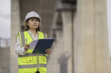 Otoyol köprüsü şantiyesinde çalışan Asyalı bir kadın mühendis inşaat çalışmalarını denetliyor.