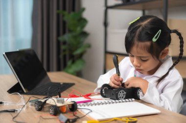 Küçük Asyalı kız STEM sınıfında robot yapıp kodluyor, mekanik oyuncak araba tamir ediyor ve tamir ediyor.