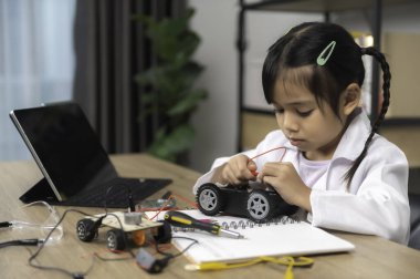 Küçük Asyalı kız STEM sınıfında robot yapıp kodluyor, mekanik oyuncak araba tamir ediyor ve tamir ediyor.