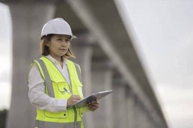 Otoyol köprüsü şantiyesinde çalışan Asyalı bir kadın mühendis inşaat çalışmalarını denetliyor.