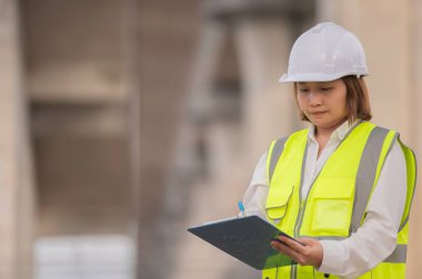 Otoyol köprüsü şantiyesinde çalışan Asyalı bir kadın mühendis inşaat çalışmalarını denetliyor.