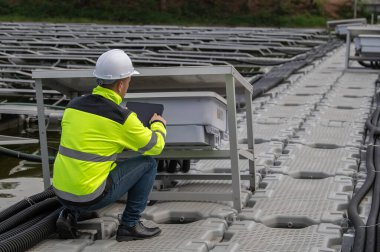 Yüzen güneş çiftliğinde çalışan mühendis, güneş panelleri yakınındaki güneş pilleriyle kontrol ve bakım yapıyor, denetleyici güneş enerjisi istasyonundaki sistemi kontrol ediyor.