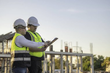Tayland 'da büyük bir inşaat projesinin şantiyesinde çalışan iki Asyalı mühendis şantiyede fazla mesai, şantiyede çalışan bir mühendis diski.