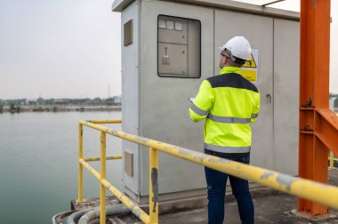 Elektrik mühendisi elektrik dağıtım kabinesinde voltajı kontrol ediyor, önleyici bakım yıllık, atık su arıtma tesisinde çalışan denetleyici
