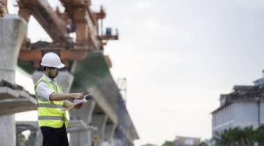 Asyalı bir erkek mühendis otoban köprüsü şantiyesinde çalışıyor, inşaat çalışmalarını denetleyen bir memur, yüksek hızlı demiryolu şantiyesinde çalışan bir denetçi.