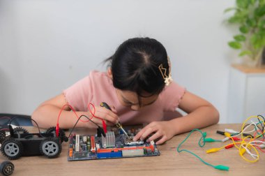 Küçük Asyalı kız STEM sınıfında robot yapıp kodluyor, mekanik oyuncak araba tamir ediyor ve tamir ediyor.