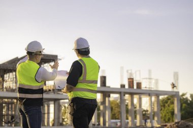 Tayland 'da büyük bir inşaat projesinin şantiyesinde çalışan iki Asyalı mühendis şantiyede fazla mesai, şantiyede çalışan bir mühendis diski.