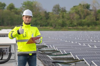 Yüzen güneş çiftliğinde çalışan mühendis, güneş panelleri yakınındaki güneş pilleriyle kontrol ve bakım yapıyor, denetleyici güneş enerjisi istasyonundaki sistemi kontrol ediyor.