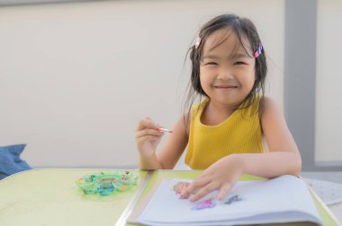 Asyalı çocuk, öğretmenlere, tatilde hobilerine ev ödevi göndermek için resim çizer ve resim yapar.