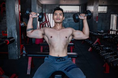 Spor salonunda çalışan yakışıklı, ağırlık kaldıran Asyalı bir adam spor müsabakası için ağırlık kaldırıyor sırt kası çalıştırmak için halteri kaldırıyor.