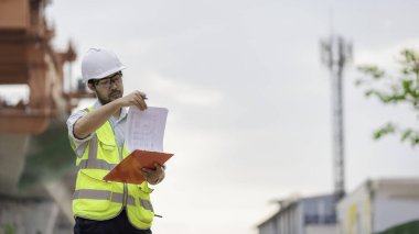 Asyalı bir erkek mühendis otoban köprüsü şantiyesinde çalışıyor, inşaat çalışmalarını denetleyen bir memur, yüksek hızlı demiryolu şantiyesinde çalışan bir denetçi.