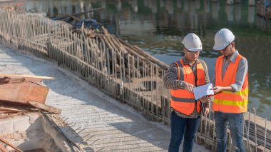 Nehir kıyısındaki bir köprü inşaatında inşaat mühendisi inşaat mühendisi, inşaat denetçisi, Foreman inşaat sahasında çalışıyor, teknik sorunları birlikte tartışıyorlar.
