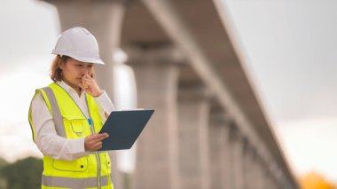 Otoyol köprüsü şantiyesinde çalışan Asyalı bir kadın mühendis inşaat çalışmalarını denetliyor.