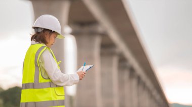 Otoyol köprüsü şantiyesinde çalışan Asyalı bir kadın mühendis inşaat çalışmalarını denetliyor.