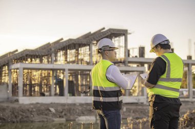 Tayland 'da büyük bir inşaat projesinin şantiyesinde çalışan iki Asyalı mühendis şantiyede fazla mesai, şantiyede çalışan bir mühendis diski.