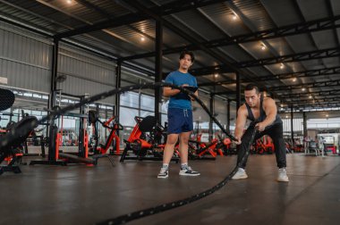 Asyalı bir adam kişisel antrenörüyle bir taburede oturuyor, ağırlık antrenmanı, vücut ve sağlıklı kardiyo sporları öğretmesi için profesyonel bir antrenör tutuyor.