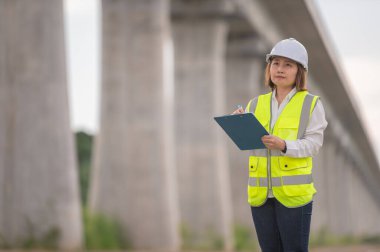 Otoyol köprüsü şantiyesinde çalışan Asyalı bir kadın mühendis inşaat çalışmalarını denetliyor.