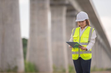 Otoyol köprüsü şantiyesinde çalışan Asyalı bir kadın mühendis inşaat çalışmalarını denetliyor.
