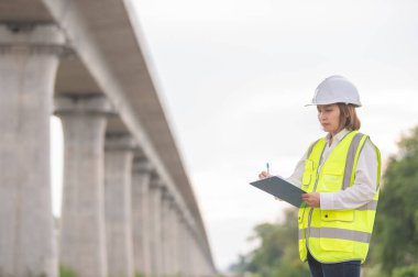 Otoyol köprüsü şantiyesinde çalışan Asyalı bir kadın mühendis inşaat çalışmalarını denetliyor.