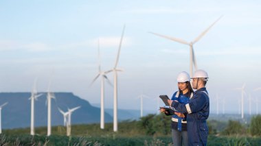 Taylandlı iki mühendis rüzgar türbini çiftliği güç jeneratörü istasyonunda çalışıyor ve raporları tutuyor. Teknisyen erkek ve kadın iş hakkında tartışıyorlar.