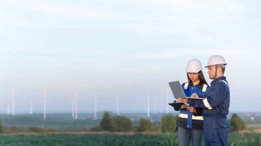 Taylandlı iki mühendis rüzgar türbini çiftliği güç jeneratörü istasyonunda çalışıyor ve raporları tutuyor. Teknisyen erkek ve kadın iş hakkında tartışıyorlar.