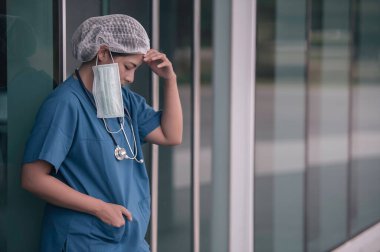Depresyonda olan Asyalı kadın hemşire yüz maskesi giyiyor mavi üniforma hastane zemininde oturuyor, genç kadın doktor sıkı çalışmaktan strese giriyor.