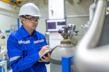 Tayland 'da, ameliyathanede çalışan Asyalı mühendis kask takıyor, özenle ve sabırla çalışıyor, hidrojen tankının valf düzenleyicisini kontrol ediyor..