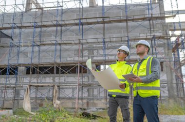 Büyük bir inşaat projesinin şantiyesinde çalışan iki Asyalı mühendis inşaat sahasında fazla mesai, inşaat alanında mühendislik diski.