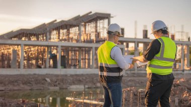 Tayland 'da büyük bir inşaat projesinin şantiyesinde çalışan iki Asyalı mühendis şantiyede fazla mesai, şantiyede çalışan bir mühendis diski.
