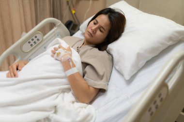 Asyalı kadın hasta ve hastanede tedavi görüyor, doktorun damar içi ilaç vermesini bekliyor, bir hemşire ateşimi ölçmek ve kan basıncımı ölçmek için geldi..
