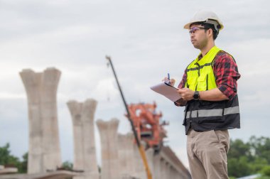 Asyalı bir erkek mühendis otoban köprüsü şantiyesinde çalışıyor, inşaat çalışmalarını denetleyen bir memur, yüksek hızlı demiryolu şantiyesinde çalışan bir denetçi.