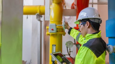 Kazan dairesinde çalışan gözlüklü Asyalı mühendis, ısıtma sistemi ekipmanlarının teknik verilerini kontrol ediyor, Taylandlılar