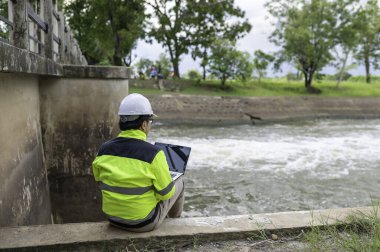 Kontrol rutinini yapan bir mühendis. Başlığı ve mühendis üniforması giyiyor. Demiryolunun kenarında duruyor. Birkaç gündür yağan şiddetli yağmurdan su seviyelerini izleyin..