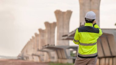 Asyalı bir erkek mühendis otoban köprüsü şantiyesinde çalışıyor, inşaat çalışmalarını denetleyen bir memur, yüksek hızlı demiryolu şantiyesinde çalışan bir denetçi.