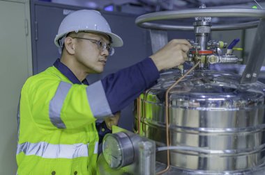 Tayland 'da, ameliyathanede çalışan Asyalı mühendis kask takıyor, özenle ve sabırla çalışıyor, hidrojen tankının valf düzenleyicisini kontrol ediyor..