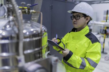 Tayland 'da, ameliyathanede çalışan Asyalı mühendis kask takıyor, özenle ve sabırla çalışıyor, hidrojen tankının valf düzenleyicisini kontrol ediyor..