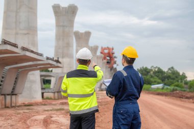 An Asian male engineer works at a motorway bridge construction site,Civil worker inspecting work on crossing construction,Supervisor working at high-speed railway construction site clipart