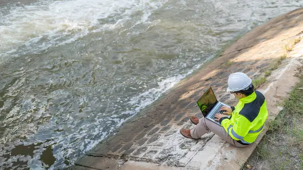 Kontrol rutinini yapan bir mühendis. Başlığı ve mühendis üniforması giyiyor. Demiryolunun kenarında duruyor. Birkaç gündür yağan şiddetli yağmurdan su seviyelerini izleyin..