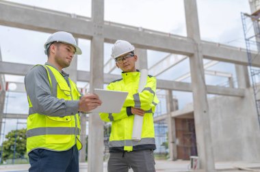 Büyük bir inşaat projesinin şantiyesinde çalışan iki Asyalı mühendis inşaat sahasında fazla mesai, inşaat alanında mühendislik diski.
