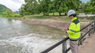 Kontrol rutinini yapan bir mühendis. Başlığı ve mühendis üniforması giyiyor. Demiryolunun kenarında duruyor. Birkaç gündür yağan şiddetli yağmurdan su seviyelerini izleyin..