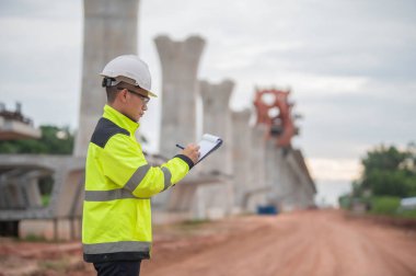 Asyalı bir erkek mühendis otoban köprüsü şantiyesinde çalışıyor, inşaat çalışmalarını denetleyen bir memur, yüksek hızlı demiryolu şantiyesinde çalışan bir denetçi.