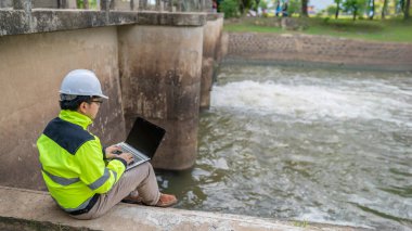 Kontrol rutinini yapan bir mühendis. Başlığı ve mühendis üniforması giyiyor. Demiryolunun kenarında duruyor. Birkaç gündür yağan şiddetli yağmurdan su seviyelerini izleyin..