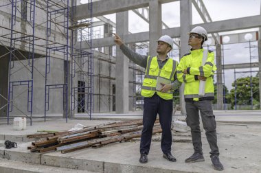 Büyük bir inşaat projesinin şantiyesinde çalışan iki Asyalı mühendis inşaat sahasında fazla mesai, inşaat alanında mühendislik diski.