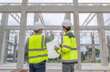 Büyük bir inşaat projesinin şantiyesinde çalışan iki Asyalı mühendis inşaat sahasında fazla mesai, inşaat alanında mühendislik diski.
