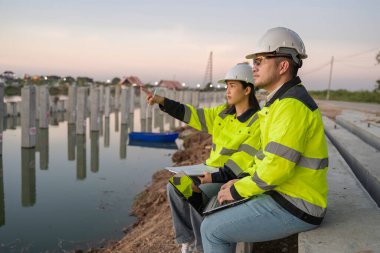 Civil Engineers Consult on Pile Driving in Water,Working at site of a large building project Construction Site Collaboration,Discuss Construction Project,Building Foundations at the Site clipart