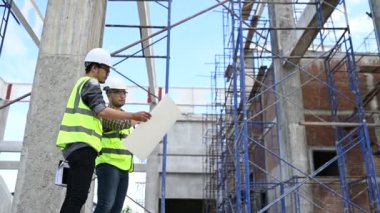 İki inşaat işçisi şantiyede duruyor ve çalışma planlarını tartışıyorlar.