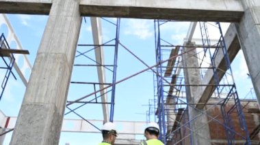 İki inşaat işçisi şantiyede duruyor ve çalışma planlarını tartışıyorlar.